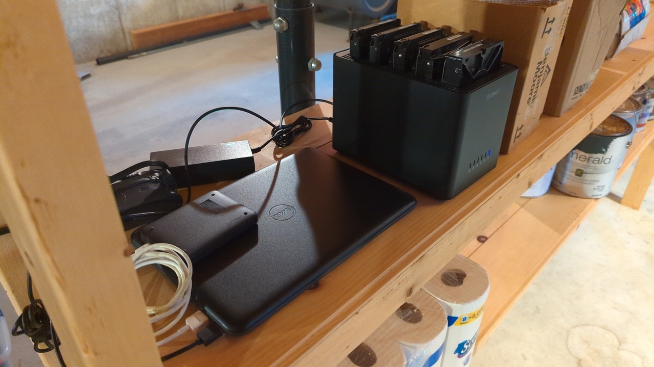 A netbook and USB drive bay with five drives attached, all sitting on a shelf in my basement