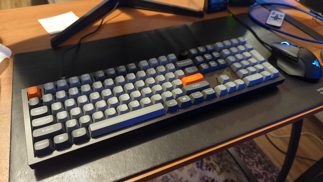 The keyboard described below sitting on my desk; the case is black, and the keycaps are mostly gray with darker gray for the modifiers and orange for escape and return